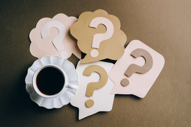 A cup of coffee and several paper cutouts of question marks placed on a table.