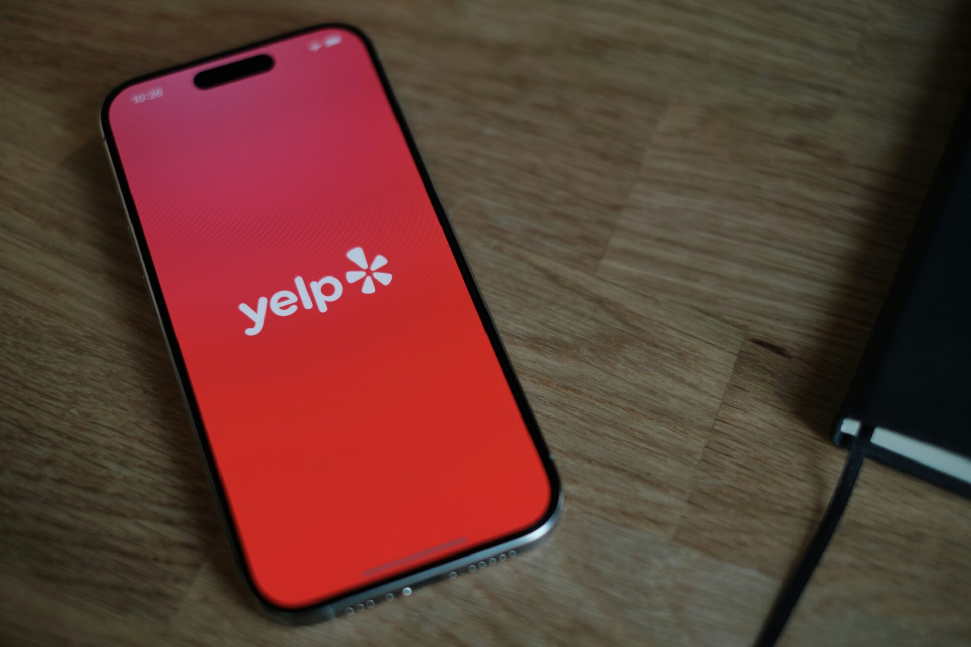 A smartphone on a wooden table with the Yelp logo on the screen